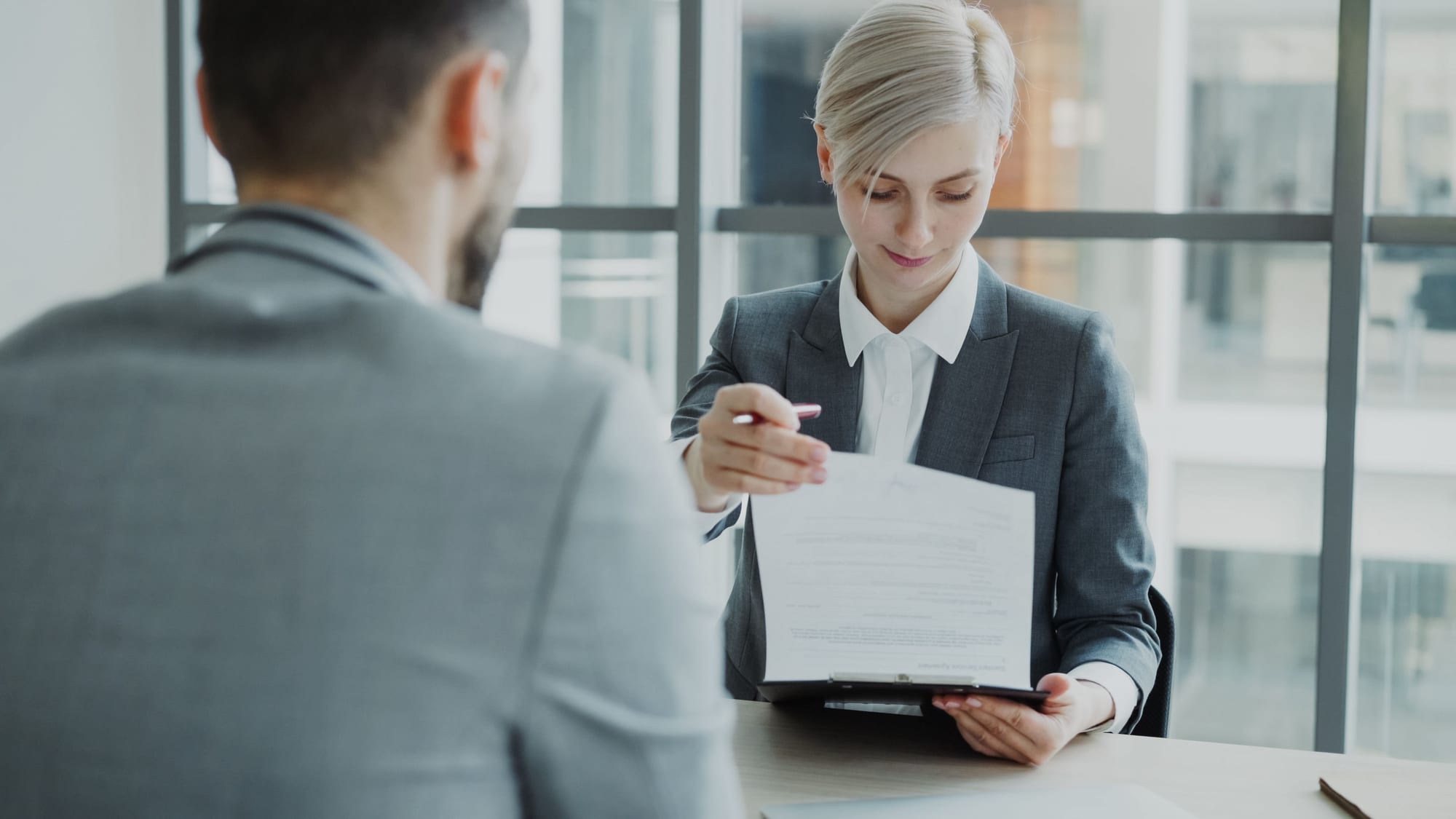 Zwei Personen besprechen gemeinsam ein Vertragsdokument an einem Schreibtisch im Büro